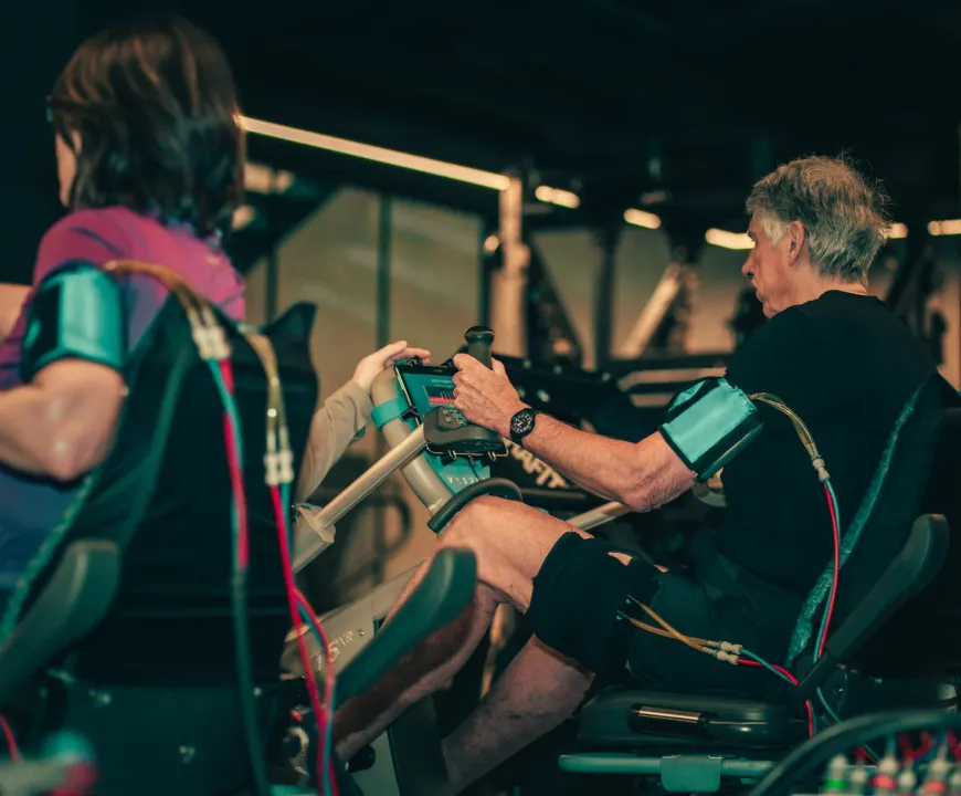 A member grips the handles of a Vasper machine while wearing recovery compression cuffs during a training session