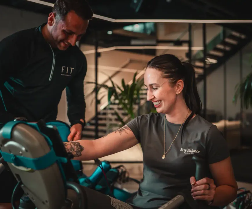 A FIT Partnership trainer guides a smiling member through a resistance machine exercise in the studio